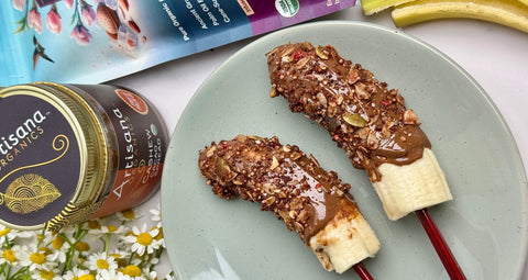 Bananas on wooden skewers covered with Cashew Cacao Spread and sprinkled with granola.