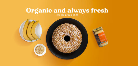 A bundt cake surrounded by bananas, a cup of oats and a jar of raw cashew butter.