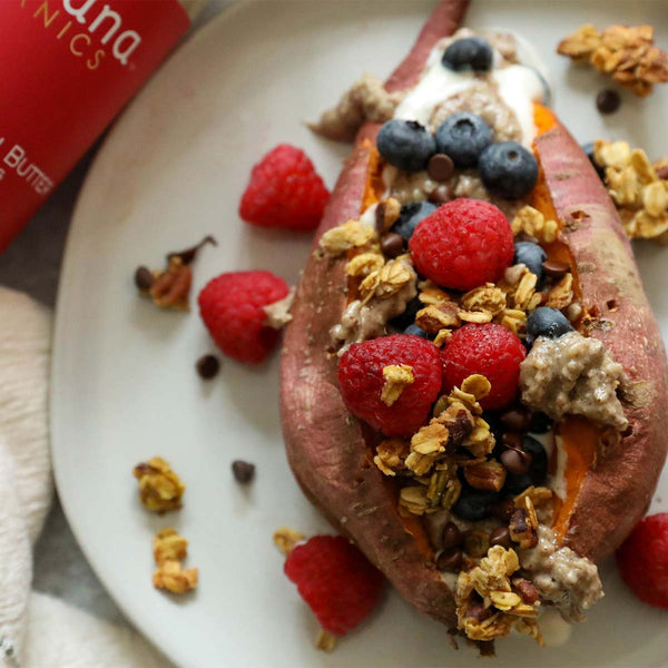 A sweet potato split on a plate and stuffed with fruit and granola.