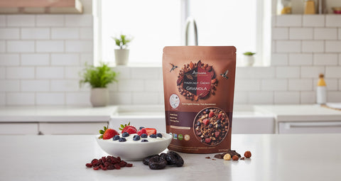 Modern white kitchen with a pouch of granola on the counter. Surrounding  is a bowl of berries and dried cranberries and dried plums.