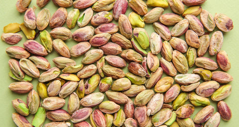 Many shelled pistachios in a single layer on a flat green surface.