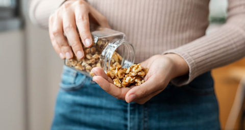 A woman getting a snack size handful of walnuts out of a glass jar.