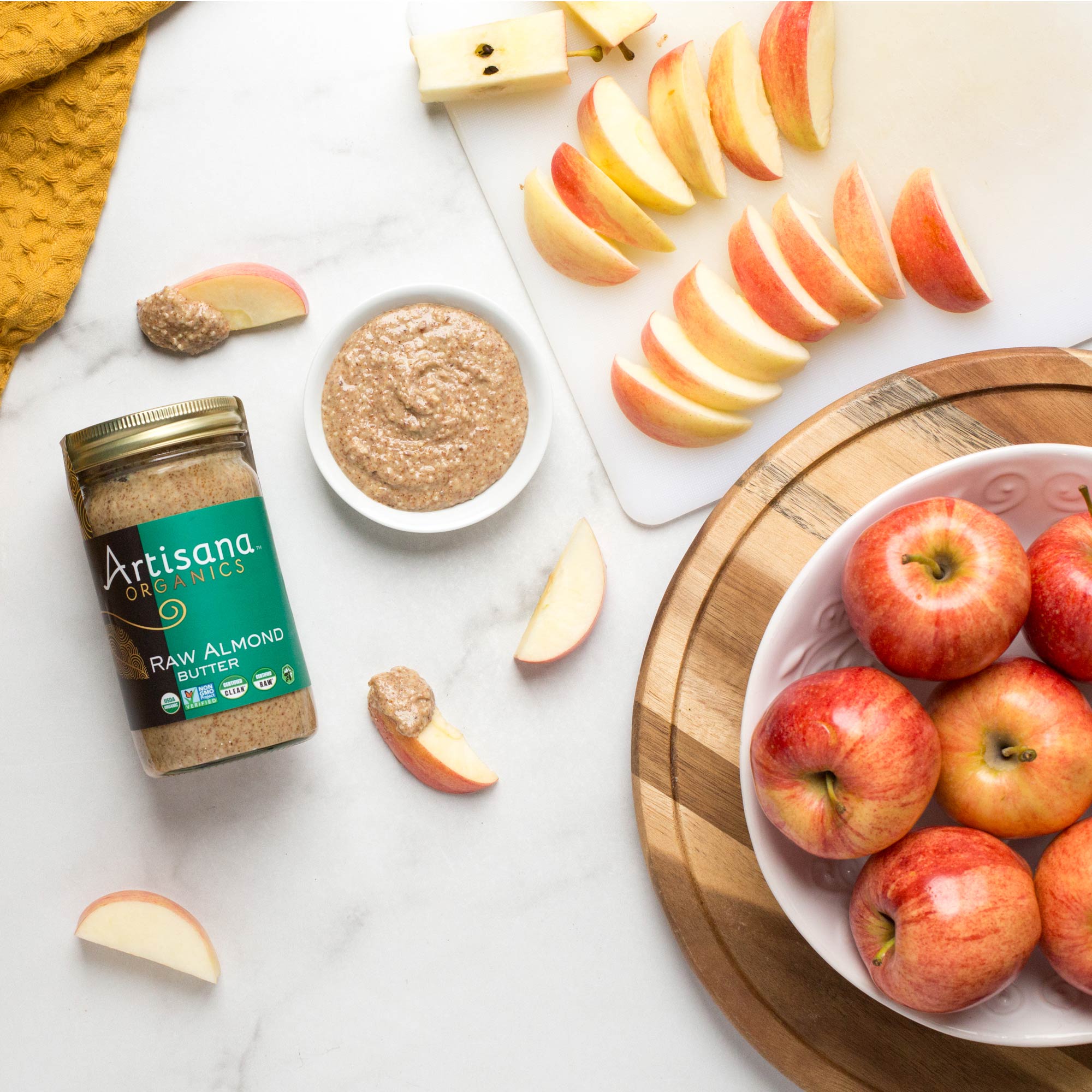 Artisana Organic raw almond butter jar with sliced apples on a marble surface