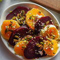 Plated salad with sliced oranges, beets, and garnished with feta and pistachios.
