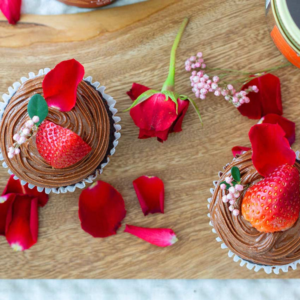 Chocolate mousse cupcakes garnished with strawberries and surrounded by rose petals. 
