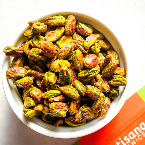 White bowl filled with green and orange roasted pistachios on a white background