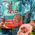 A person holding a handful of coconut granola with dried berries outdoors.