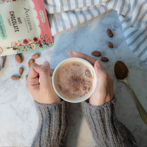 Hands in a cozy sweater holding a mug of Artisana Hot Chocolate.