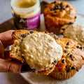 Muffin with macadamia cashew butter with more muffins and a jar of nut butter in the background.