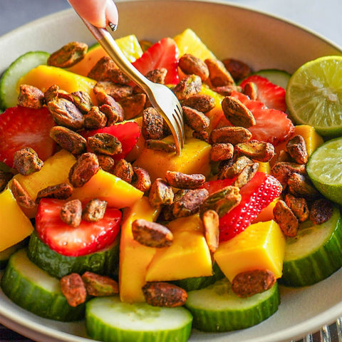 Fruit salad with strawberries, mangoes, cucumbers, and pistachio nuts in a bowl with a fork.