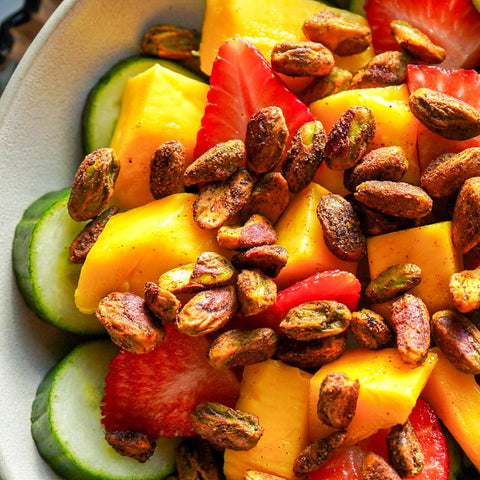 Fruit salad with mango, strawberries, and pistachios on a white plate.