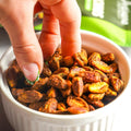 Hand reaching into a bowl pistachios with a blurred green background