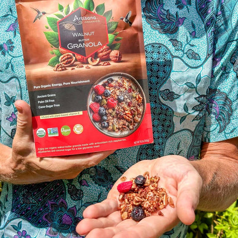 A man in a paisley shirt holding a handful of walnut granola with dried berries.